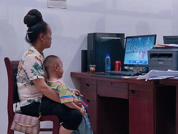 一位母亲和孩子挤不进看台，选择在村委会的电脑上看直播。澎湃新闻记者 胡杰 图