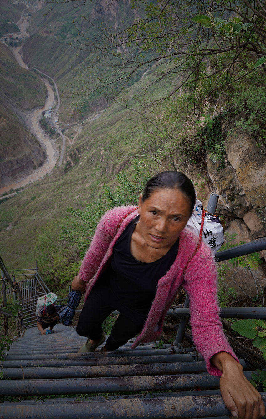 2019年5月28日，四川凉山，吉莫石普在攀爬钢梯，为家里运生活物资，身后的丈夫某色拉比是在“悬崖村”酿玉米酒的第一人